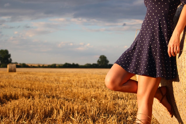 Dievča v modrých bodkovaných šatách je opreté o stoh slamy s pokrčeným kolenom