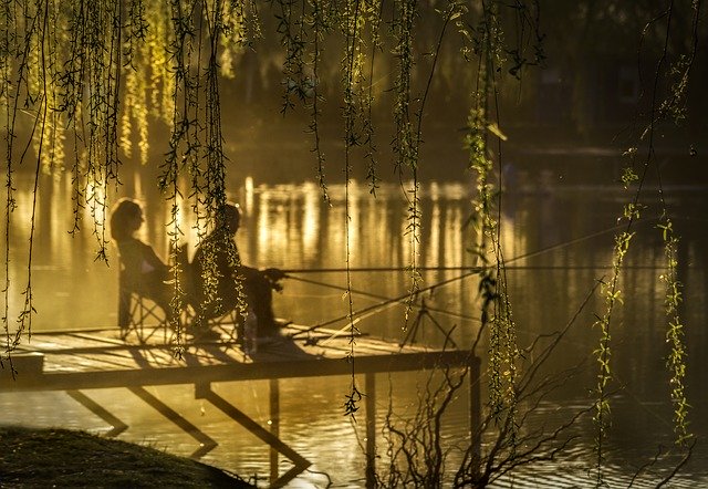 Muž a žena sedia na móle a lovia ryby pri západe slnka.jpg