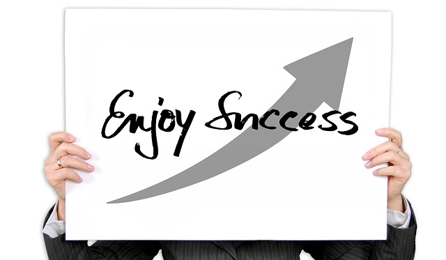 Osoba drží v rukách tabuľku s nápisom „enjoy success“ a šípkou smerujúcou nahor.jpg